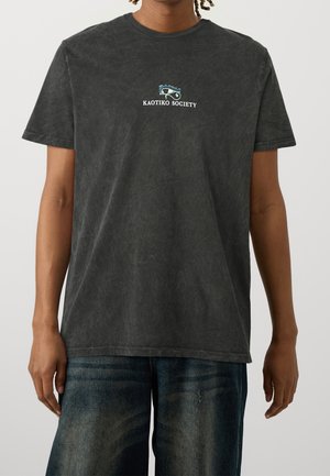 Schwarzes Grafik-T-Shirt aus Baumwollstoff mit verblasster Textur. Auf der Vorderseite befindet sich ein kleines Logo "KAOTIKO SOCIETY" in Weiß und Blau über einem Design.