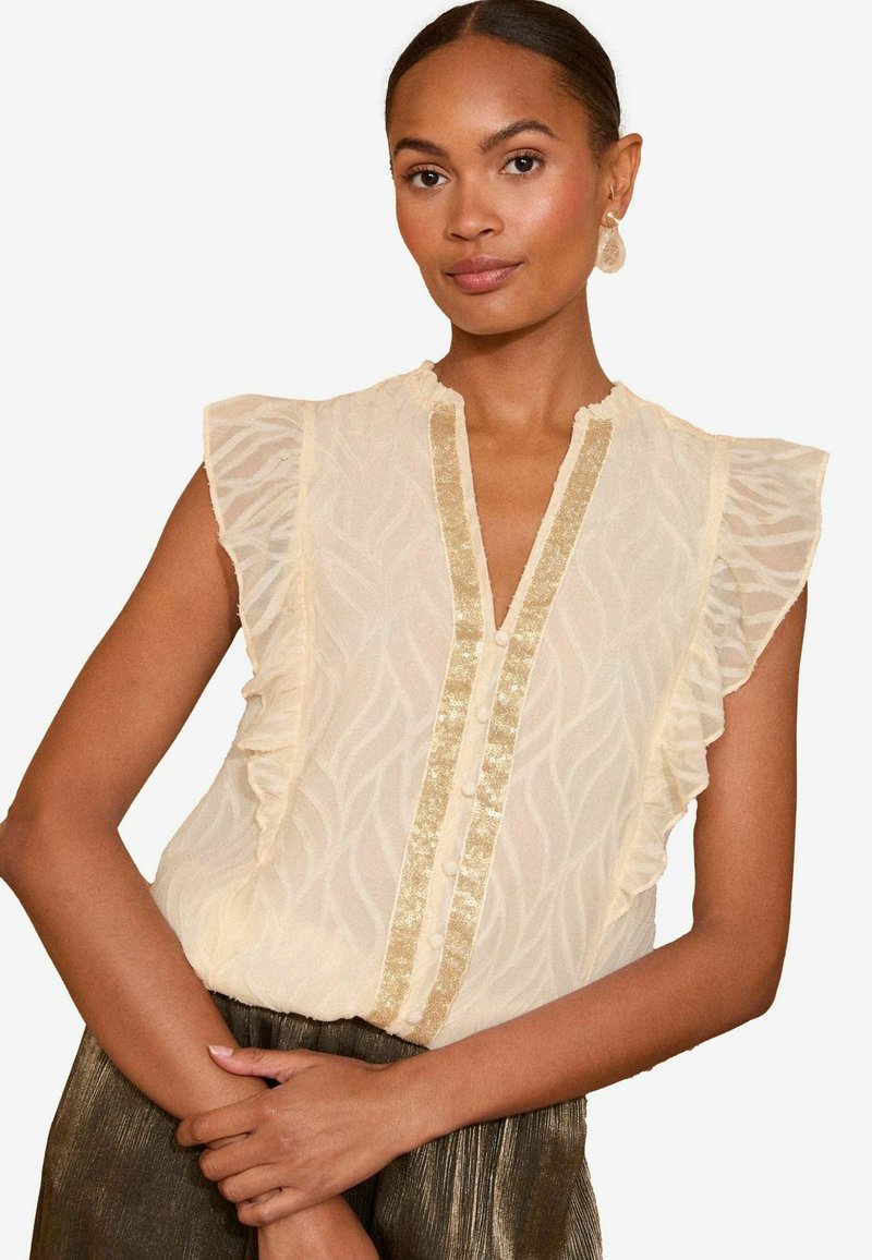 Blouse crème clair avec un motif en vagues texturé, des manches volantées et un panneau central en sequins dorés avec des boutons.