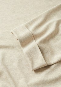 Tissu en coton beige présentant un revers roulé avec une texture lisse et un motif tacheté subtil. Doux, léger avec un design décontracté.