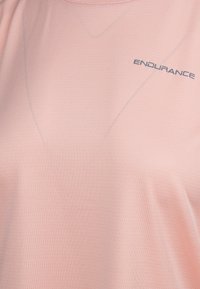 Lys lyserød sportstrøje lavet af struktureret stof. Har en rund halsudskæring og "ENDURANCE" logo i mørkegrå på forsiden.