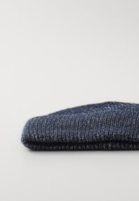 Berretto in lana di un blu navy scuro con una texture a coste e un risvolto, caratterizzato da un filo metallico sottile per un tocco di dettaglio in più.