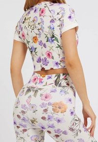 Bloemmotief crop top en legging set. Het materiaal is rekbaar, met een witte basis en kleurrijke bloemen in verschillende tinten.