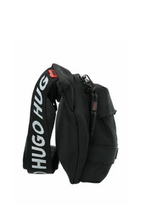 Borsa a spalla nera con design imbottito, tessuto texturizzato, tracolla regolabile con il testo "HUGO". Presenta una chiusura zip e scompartimenti laterali.