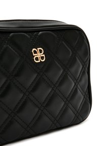 Bolso de piel negra acolchada con una textura suave, que presenta un detalle de logo dorado y patrones de costura en diagonal en la superficie.