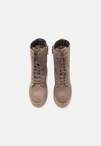 Para brązowych zamszowych butów zapinanych na sznurowadła z grubymi gumowymi podeszwami i zamkami błyskawicznymi z boku, widok z góry na białym tle.