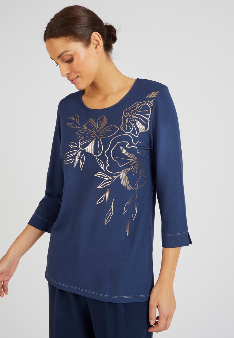 T-shirt à manches longues bleu marine avec une broderie florale métallisée dorée sur le devant. Présente un col rond et un subtil détail de couture.