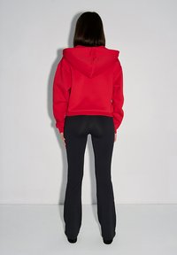 Rote Kapuzenjacke mit Kordelzugkapuze, kombiniert mit schwarzen Schlaghosen. Die Kapuzenjacke hat eine lässige Passform und eine weiche Textur.