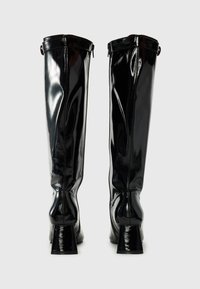 Bottes noires brillantes jusqu'aux genoux avec un talon carré, texture lisse et fermeture à glissière à l'arrière. Présente un bout rond et un design élégant.