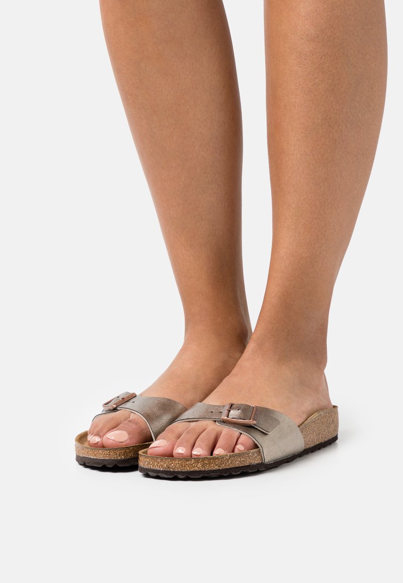 Brune skinnsandaler med bred stropp, med en metallspenne, korkfotseng og strukturerte gummisåler. Tærne er synlige.