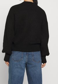 Svart ribbad stickad tröja med rund hals och lösa ärmar, kombinerad med ljusblå högmidjade jeans i denim med bakfickor.