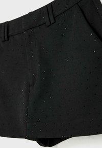 Crne hlače kratke duljine od teksturiranog materijala, ukrašene sitnim sjajnim ukrasima, s ravnim prednjim dijelom s prorezima za remen i krojem po mjeri.