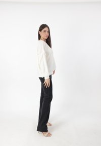 Witte gebreide trui met oversized mouwen, gecombineerd met zwarte broek en beige sandaaltjes met hakken. Soepele textuur, relaxed fit.