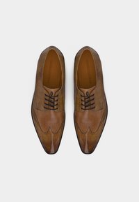 Ζευγάρι καφέ δερμάτινα παπούτσια φόρμας με μοτίβο κροκοδείλου και μαύρα κορδόνια, φωτογραφημένα από πάνω σε λευκό φόντο.