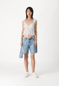 White floral-patterned crop top with ruffled sleeves, paired with light blue denim shorts and white sneakers, holding a small blue bag.