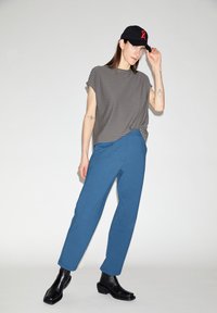 Gestreept grijs en wit shirt met korte mouwen, blauwe broek, zwarte enkellaarzen en een zwarte pet met een rood lintlogo. Eenvoudig modern ontwerp.