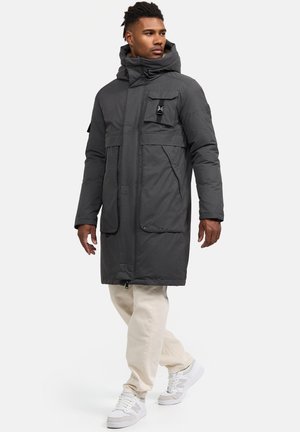 Parka aislante de color gris oscuro con un cuello alto, cierre de cremallera, bolsillos frontales y capucha ajustable, combinada con pantalones beige y zapatillas blancas.
