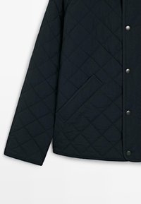Quiltet sort jakke med trykknaplukning, sidelomme og tekstil med diamantmønster på overfladen.