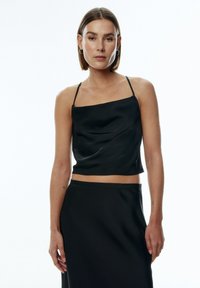 Zwarte satijnen camisole met dunne spaghettibandjes, met een licht gedrapeerd ontwerp en een cropped lengte. Gladde textuur met een minimalistische stijl.