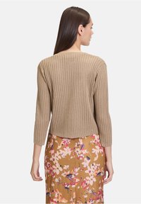 Khakifarbenes, geripptes Sweatshirt mit Dreiviertelärmeln; verfügt über ein strukturiertes Strickmuster und ein kurzes Design. Musterröcke mit Blumenmuster.