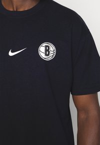 Camiseta de algodón azul marino con un logo blanco de Nike y un gráfico de baloncesto con un emblema "B" en el pecho. Mangas cortas, ajuste clásico.