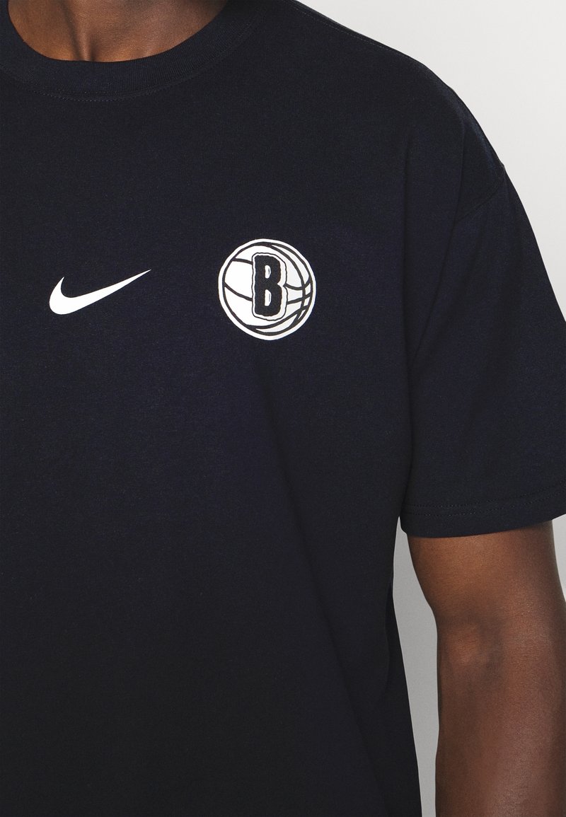 Camiseta de algodón azul marino con un logo blanco de Nike y un gráfico de baloncesto con un emblema "B" en el pecho. Mangas cortas, ajuste clásico.