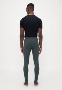 Musta lyhythihainen paita ja vihreät tiukat legginsit. Legginsseissä on nilkkaleikkaukset. Sileä pinta, vartalonmyötäinen muotoilu ja venyvä materiaali.