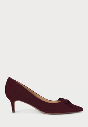 Décolleté in suede bordeaux con punta affilata, tacco basso e un fiocco annodato sul puntale; texture liscia e design elegante.