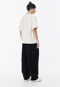 T-shirt beige a maniche corte abbinata a pantaloni neri larghi. Il modello indossa un berretto a coste scuro e sneaker bianche.