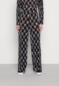 Czarno-białe plisowane spodnie w patterny o luźnym, szerokim kroju, z abstrakcyjnymi wzorami i gładką teksturą. Połączone z czarnymi butami.