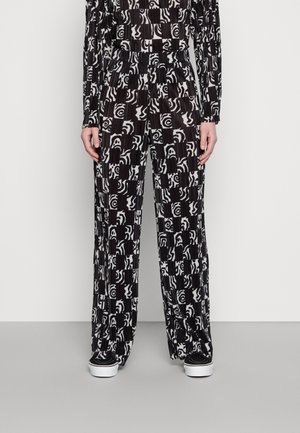 Czarno-białe plisowane spodnie w patterny o luźnym, szerokim kroju, z abstrakcyjnymi wzorami i gładką teksturą. Połączone z czarnymi butami.