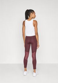 Ribbed white tank top paired with maroon leggings featuring mesh accents and white sneakers. Focus on a fitted design and breathable material.