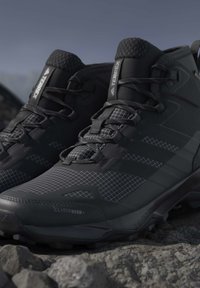 Pair of black Adidas Terrex hiking shoes with Climawarm technology, worn on rocky terrain.
