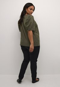Blouse en coton vert olive avec des manches bouffantes, col rond et coupe décontractée. Associée à un jean skinny noir et des ballerines noires.