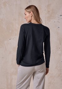 Svart långärmad tröja med rund halsringning och slät yta, i kombination med ljusgrå sweatpants. Enkelt mönster och avslappnad passform.