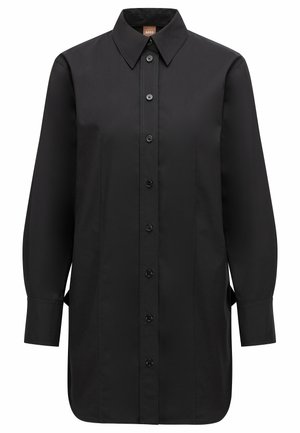 Schwarzes Langarmshirt mit spitzem Kragen, Knopfleiste auf der Vorderseite, dezenten tonalen Nähten und seitlichen Schlitzen für mehr Bewegungsfreiheit.