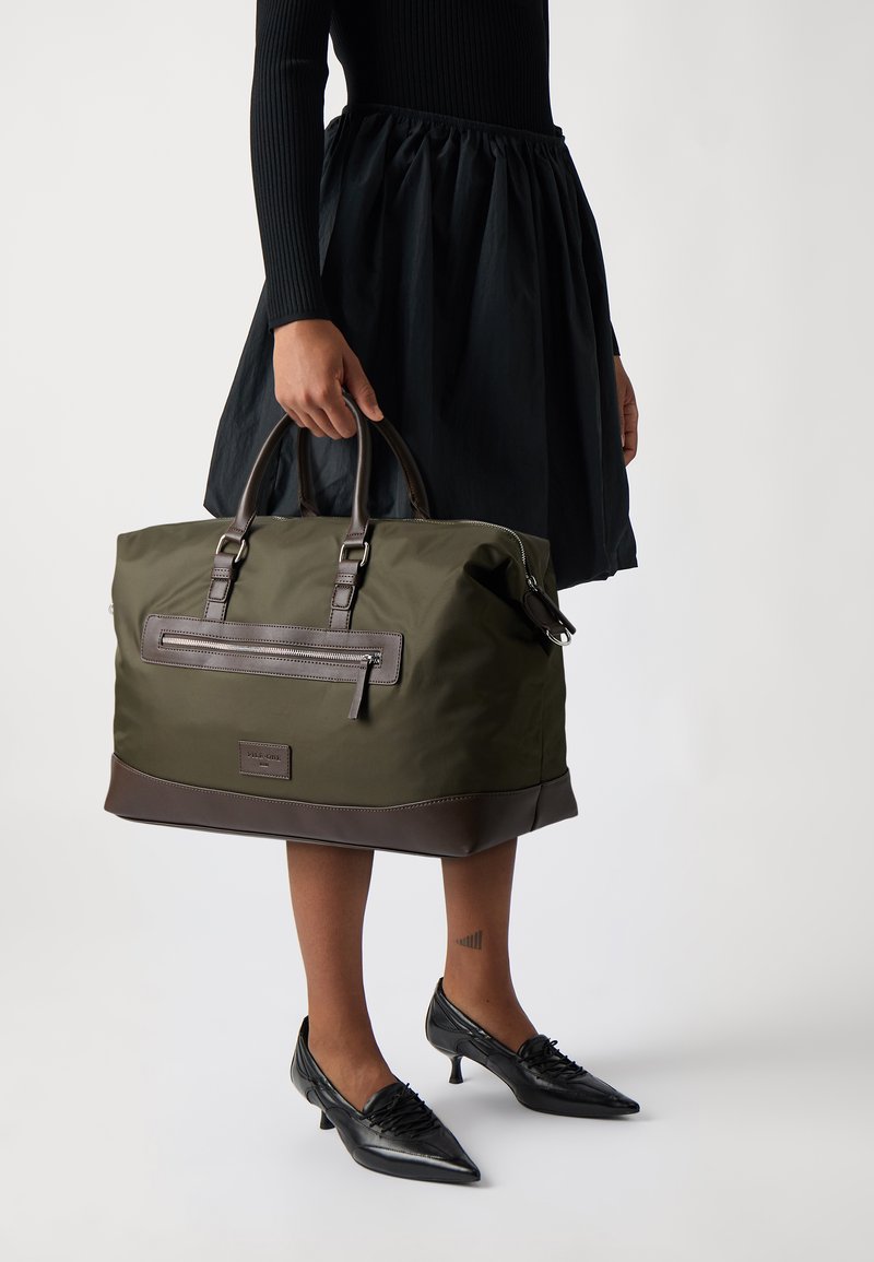 Olive green duffel bag with brown leather accents, top handles, and front zippered pocket. Smooth and durable fabric, spacious design.