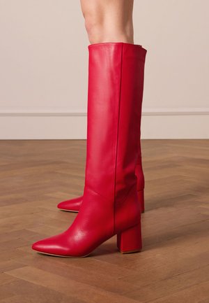 Red leather knee-high boots with a pointed toe and chunky block heel. The surface is smooth, featuring minimal stitching details.