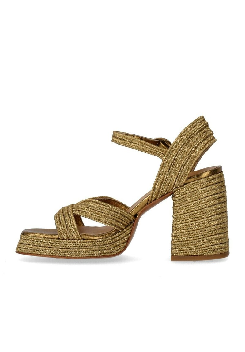 Χρυσές πλεκτές πλατφόρμες με παχιά μπλοκ τακούνι, διασταυρούμενες ταινίες και λείο πέλμα. Υφή με γυαλιστερή εμφάνιση.