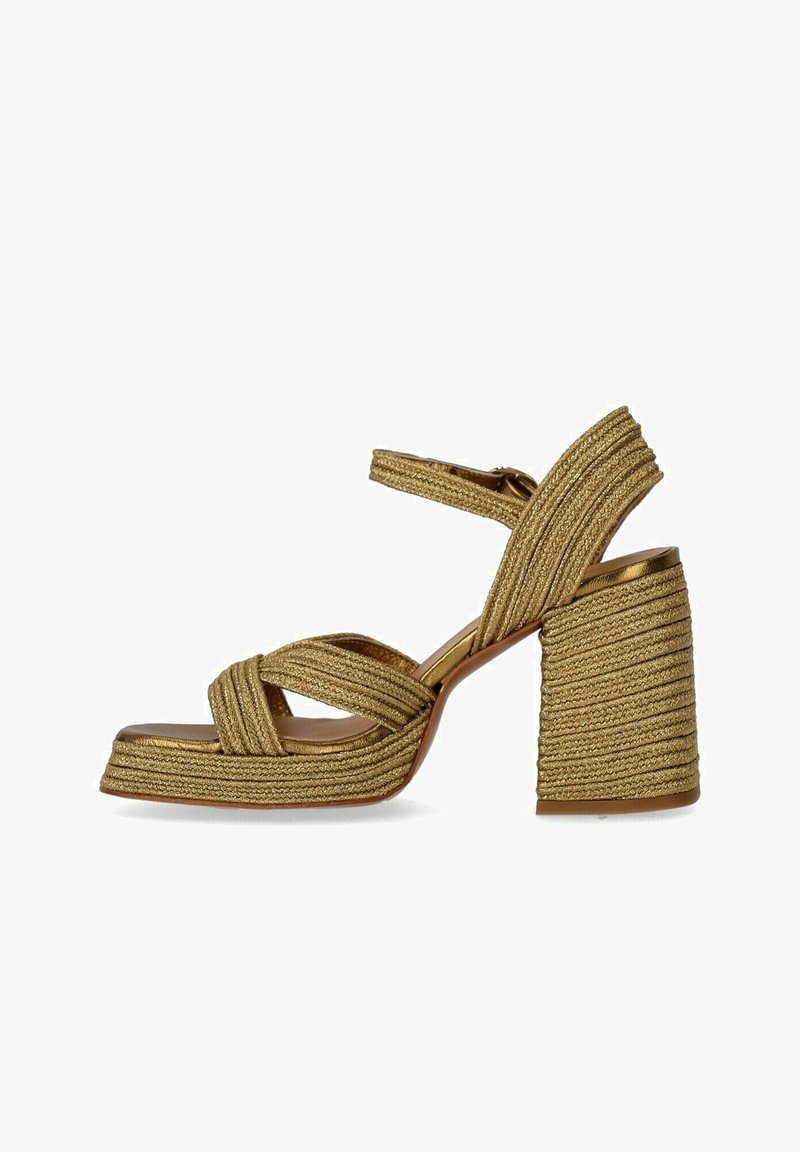 Χρυσές πλεκτές πλατφόρμες με παχιά μπλοκ τακούνι, διασταυρούμενες ταινίες και λείο πέλμα. Υφή με γυαλιστερή εμφάνιση.