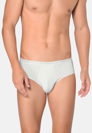 Mannelijke torso gekleed in witte low-rise slips met een elastische tailleband met het Sloggi-logo, staand tegen een effen lichte achtergrond.