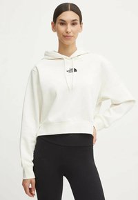 Biała krótka bluza z kapturem i sznurkiem oraz małym czarnym logo. Połączona z czarnymi, prążkowanymi legginsami, które mają luźny krój.