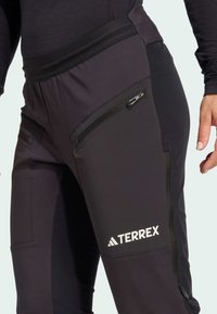 Černé sportovní kalhoty s kapsami na zip, přiléhavým střihem a elastickým pasem. Logo značky "TERREX" vyjímečně zobrazené.