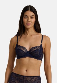 Mörk marinblå spetsbehå med byglar, vågiga kanter, justerbara band och guldfärgade detaljer. Genomskinligt tyg med blommönster.