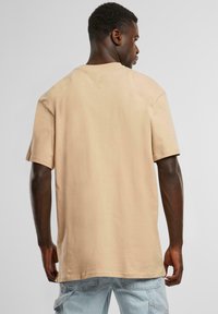 Beige cotton t-shirt with short sleeves, a crew neck, and a relaxed fit. Visible stitching along the hem and shoulder seams.