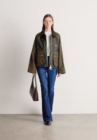 Khaki and dark green jacket with oversized sleeves and large pockets, paired with flared blue jeans and a brown handbag. Smooth texture.