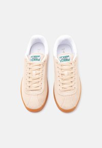 Ζευγάρι μπεζ σουέντ παπούτσια τένις Lacoste με σόλες από καουτσούκ, εκρού κορδόνια και λευκά επενδυμένα περιλαίμια, σε θέα από πάνω, πάνω σε λευκό φόντο.