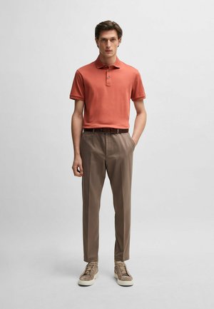 Rust-colored polo shirt, khaki pants, and taupe sneakers. Polo has a collar and three buttons; pants are tailored with a smooth texture.