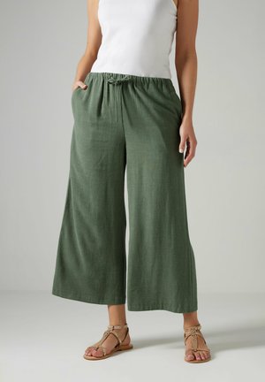 Pantaloni larghi verdi con elastico in vita e cordoncino. Realizzati in tessuto testurizzato, abbinati a sandali flat con dettagli intrecciati.