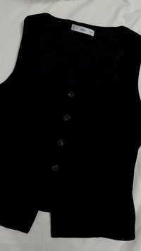 Crni bezrukavnik s glatkom teksturom, sadrži šest okruglih dugmadi sprijeda i oznaku u području vrata.