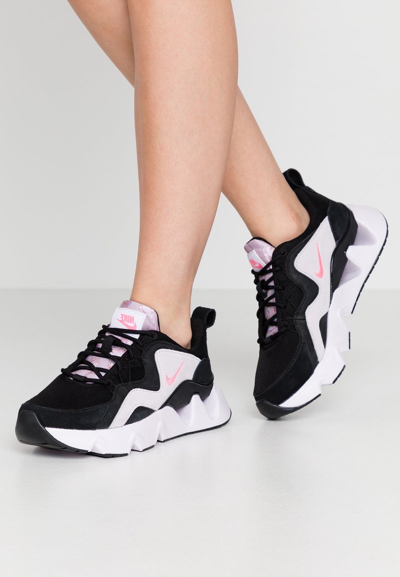 Chaussures de sport noires et roses avec une tige texturée, une semelle blanche épaisse à design géométrique et des accents de logo Nike roses.